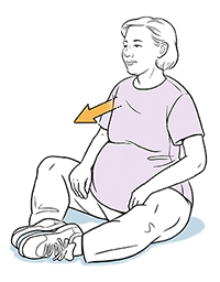 Mujer embarazada sentada en el suelo en posición de sastre.