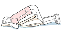 Person lying on stomach with pillows under head and abdomen.