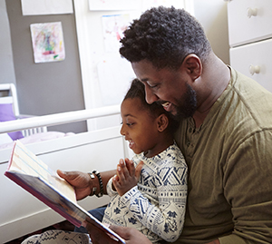 Man reading book to toddler boy sitting in his lap.