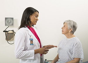 Woman sitting on exam table in doctor's office listening to doctor.