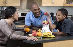 Two adults and a teen making fruit smoothies.