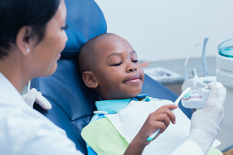 Una proveedora de atención dental le muestra a un niño cómo cepillarse los dientes.