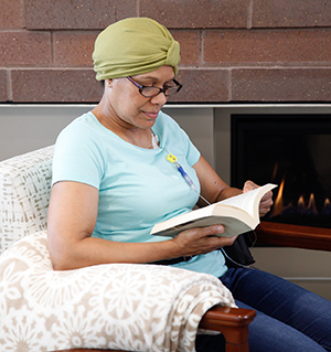 Mujer sentada en su casa, leyendo, con un puerto de infusión de quimioterapia en el pecho.